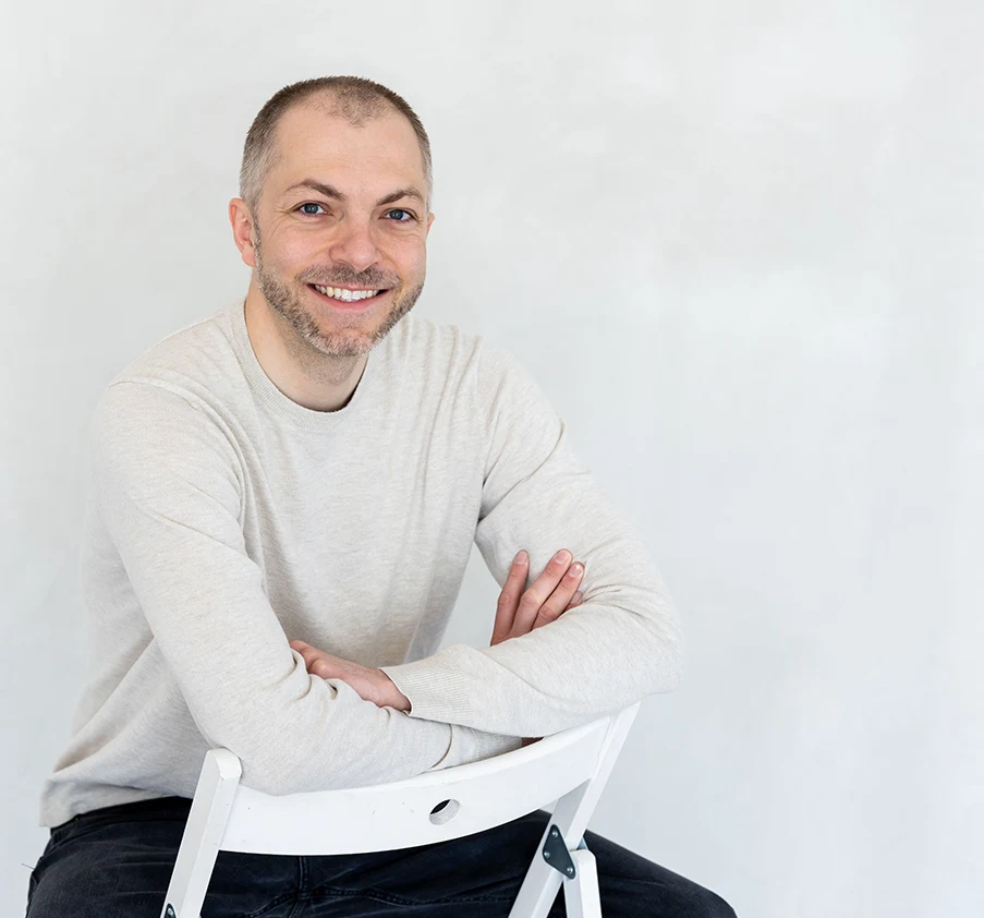 Kyle Barth, MS, LMFT, smiling, seated on a white chair